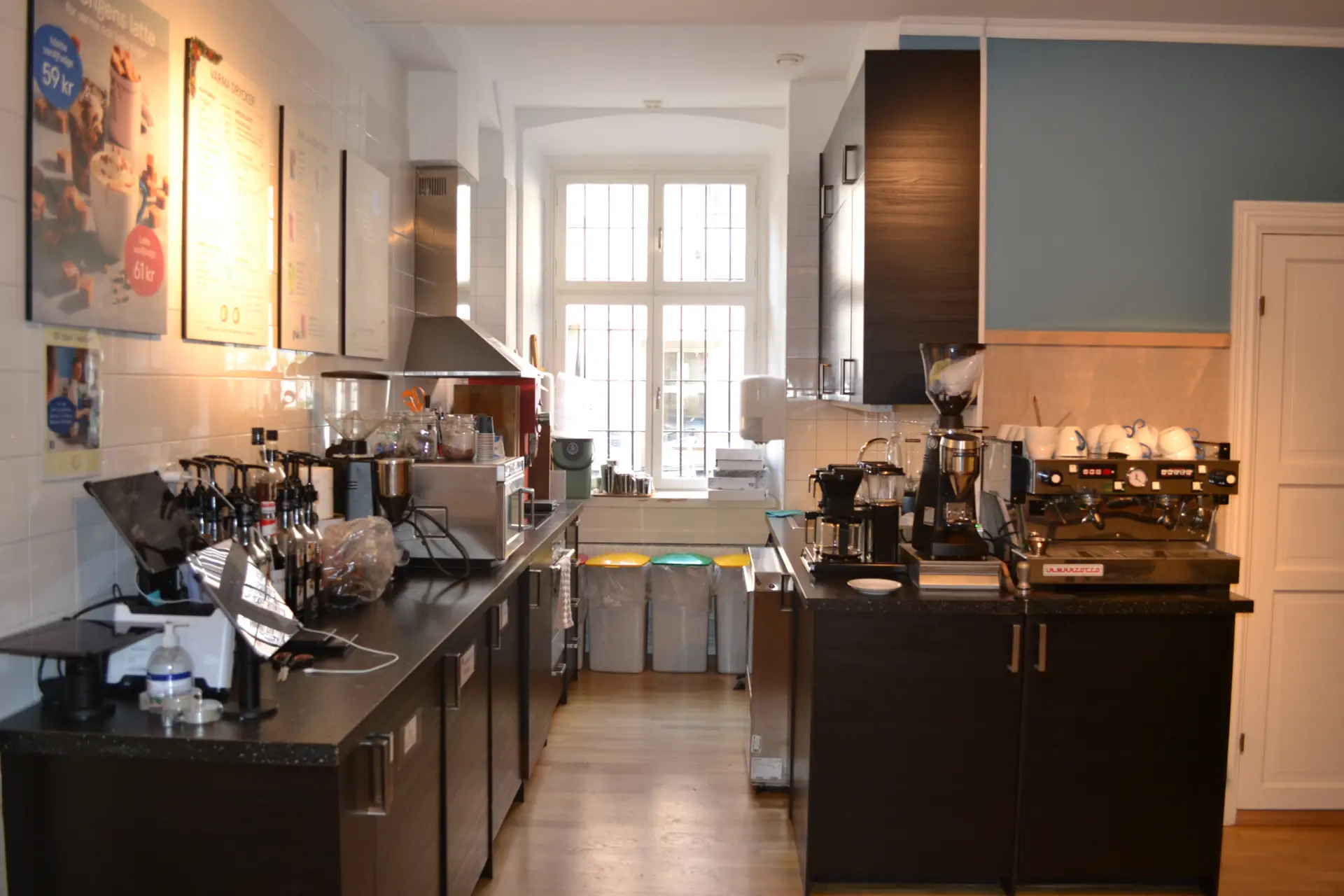 Interiör i ett mysigt kafékök med espressomaskiner, kvarnar och andra köksapparater som tar upp stora delar av köksbänkarna.